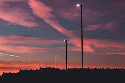 Himmel i rosa och blå nyanser och tända gatulampor. Lamporna lyser över ett mörkt villaområde.