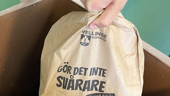 Hand håller i brun matavfallspåse på väg ned i ett kärl för matavfall.