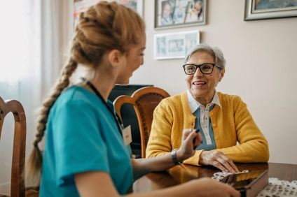 Kvinna i blond, lång fläta sitter vänd mot korthårig senior kvinna vid ett matbord.