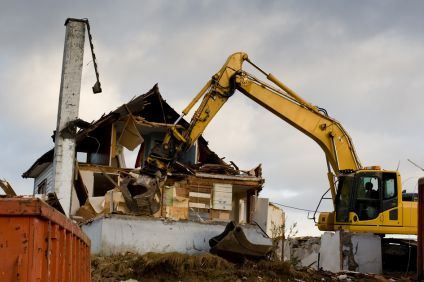 En gulfärgad grävskopa river ett enbostadshus.