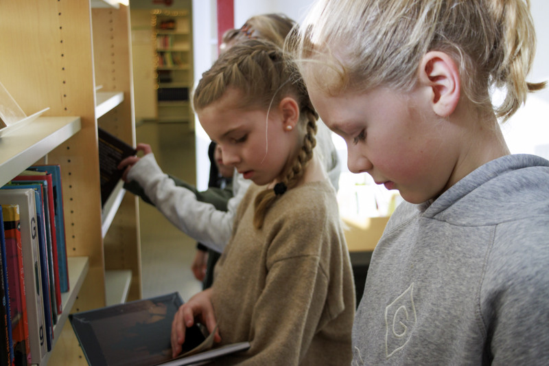 Två unga flickor tittar på en bok i ett bibliotek.