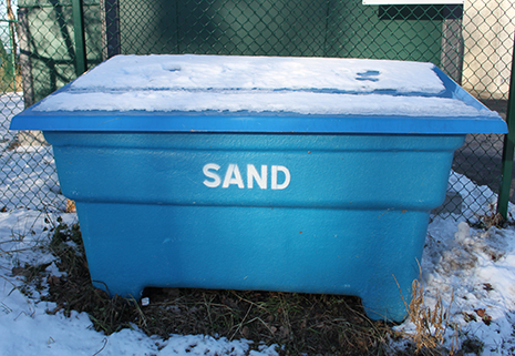 Blå låda med texten sand står i snö.