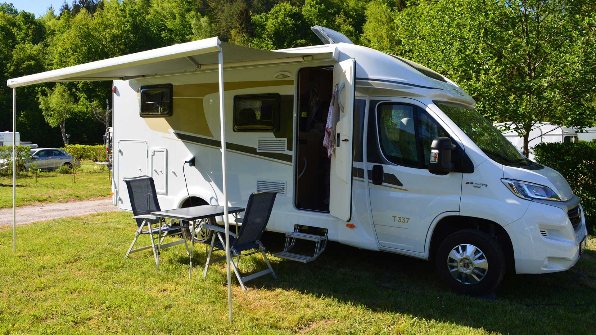 Husbil med campingset med bord och stolar i svart intill. Husbilen står på en campingplats.