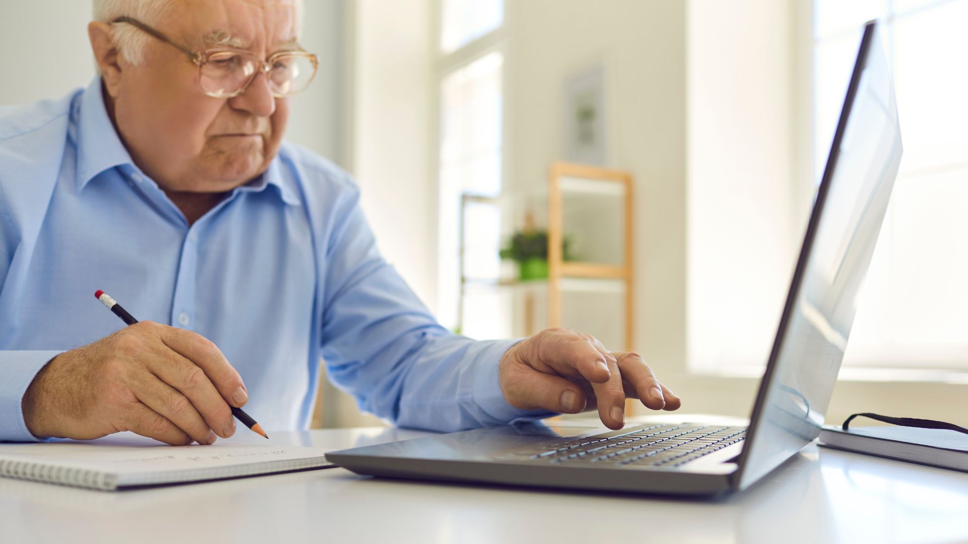 Man i ljusblå skjorta sitter med laptop och skrivblock framför sig.